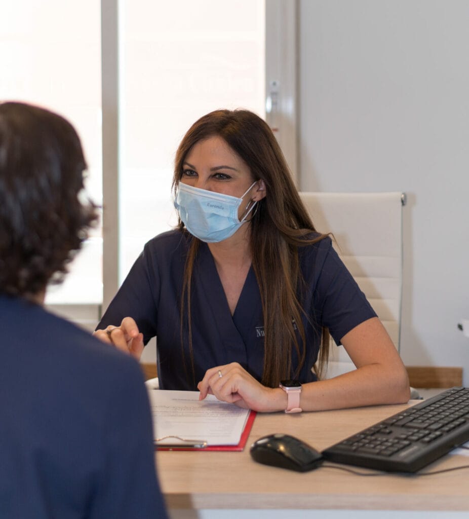 Paciente sentada en la consulta hablando con una empleada rellenando datos